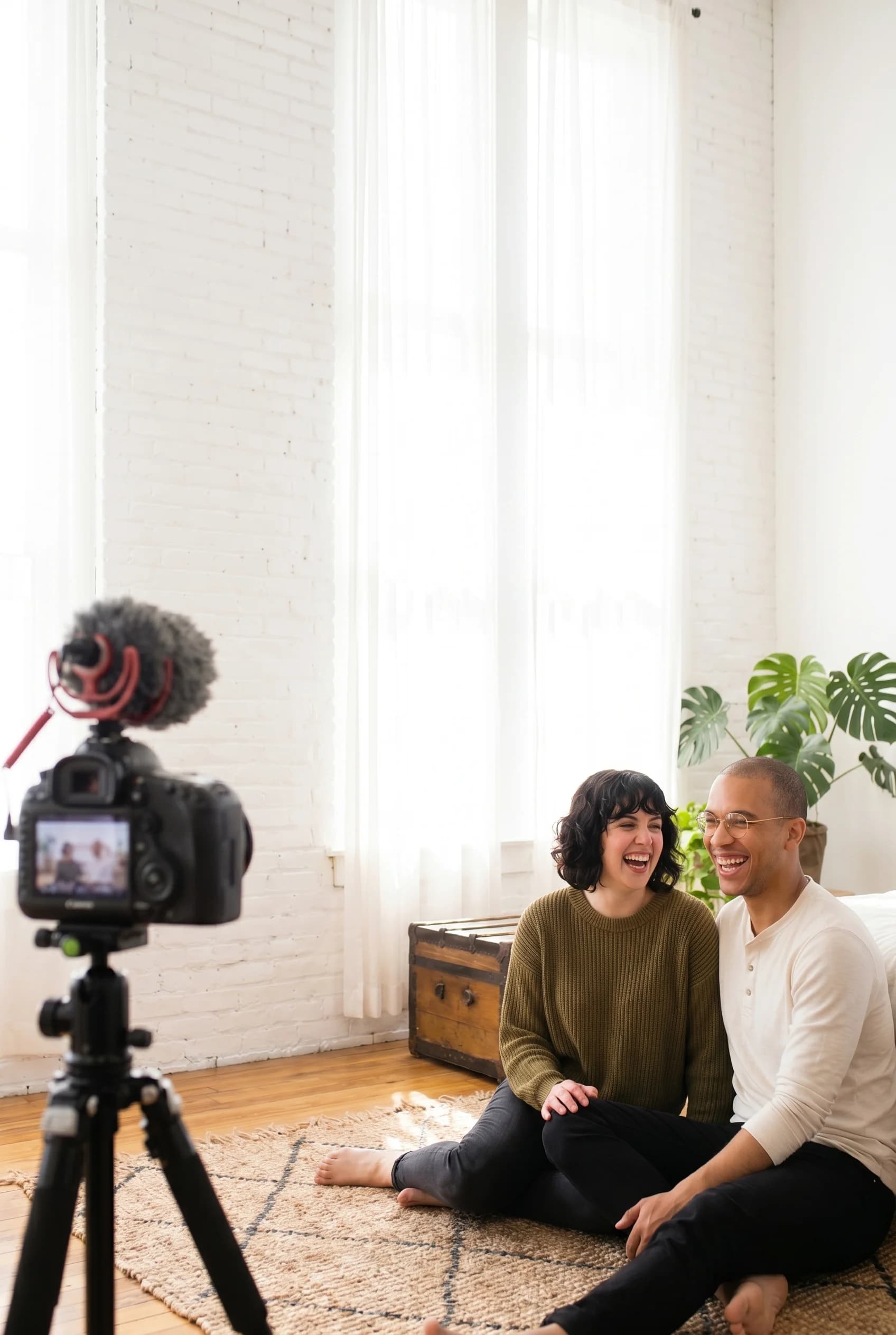 Two creators laughing together on the right while filming in a bright home YouTube studio